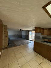 Kitchen featuring brown cabinets, a wainscoted wall, light tile patterned flooring, ceiling fan, and open floor plan