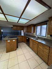 Kitchen featuring brown cabinetry, electric range oven, light tile patterned floors, and black dishwasher