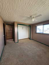 Unfurnished bedroom featuring a closet, light colored carpet, ceiling fan, and a textured ceiling