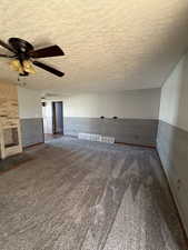 Unfurnished living room featuring a textured ceiling, a fireplace, carpet, ceiling fan, and wooden walls