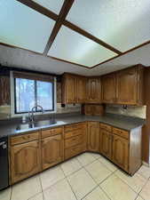 Kitchen with a textured ceiling, brown cabinetry, light tile patterned flooring, and dishwasher