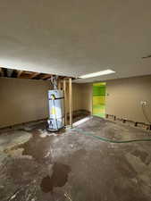 Unfinished below grade area featuring water heater and a textured ceiling
