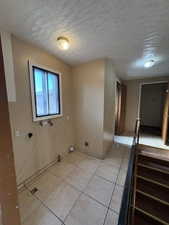 Laundry area featuring a textured ceiling, light tile patterned floors, washer hookup, and electric dryer hookup