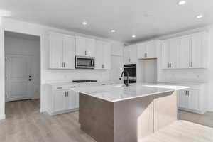 Kitchen with a center island with sink, white cabinets, recessed lighting, light wood-style floors, and light stone countertops