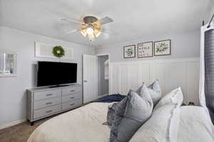 Carpeted bedroom with a ceiling fan, a textured ceiling, a wainscoted wall, and a decorative wall