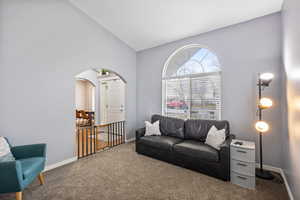Living area featuring vaulted ceiling, carpet floors, and arched walkways