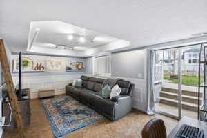 Tiled living area featuring a decorative wall, a wainscoted wall, stairway, a textured ceiling, and a tray ceiling