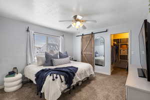 Bedroom featuring a barn door, a walk in closet, carpet floors, a textured ceiling, and ceiling fan