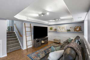 Living area featuring a raised ceiling, stairs, a textured ceiling, a decorative wall, and wainscoting
