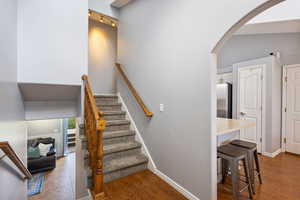 Staircase with arched walkways, wood finished floors, rail lighting, and a high ceiling