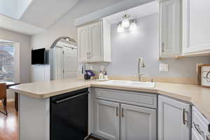 Kitchen featuring black dishwasher, a peninsula, light countertops, lofted ceiling, and white cabinets