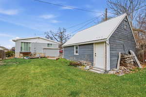 Rear view of house featuring a yard, an outdoor structure, and a metal roof