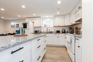 Kitchen featuring white appliances, white cabinets, light stone counters, recessed lighting, and light wood-type flooring