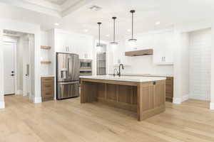Kitchen featuring brown cabinets, white cabinets, stainless steel appliances, an island with sink, and open shelves
