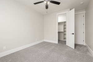 Unfurnished bedroom with light colored carpet, a spacious closet, and a ceiling fan