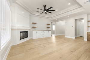 Unfurnished living room with a glass covered fireplace, light wood-type flooring, a tray ceiling, recessed lighting, and ornamental molding
