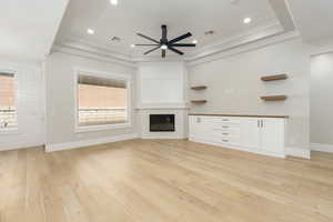 Unfurnished living room featuring a glass covered fireplace, light wood-style flooring, crown molding, ceiling fan, and recessed lighting