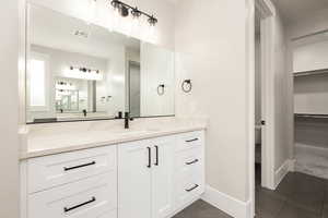 Full bath featuring vanity, a walk in closet, and dark tile patterned floors
