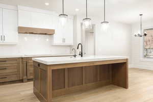 Kitchen with brown cabinetry, light wood-type flooring, pendant lighting, white cabinetry, and recessed lighting