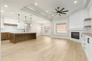 Kitchen with white cabinets, a glass covered fireplace, brown cabinets, a large island, and light wood-style floors