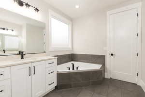 Bathroom with a garden tub, vanity, dark tile patterned flooring, and recessed lighting