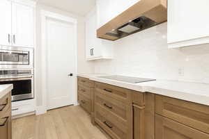 Kitchen featuring stainless steel appliances, custom exhaust hood, light wood-style flooring, white cabinets, and light stone countertops