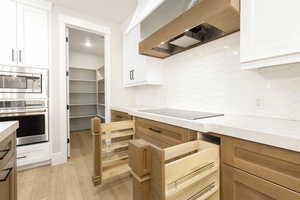 Kitchen featuring custom exhaust hood, appliances with stainless steel finishes, white cabinetry, light wood-style floors, and light stone counters