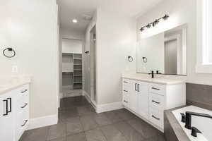 Full bath featuring vanity, a walk in closet, a relaxing tiled tub, dark tile patterned flooring, and recessed lighting