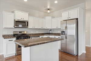 Kitchen with white cabinetry, appliances with stainless steel finishes, dark wood-style flooring, dark stone counters, and recessed lighting