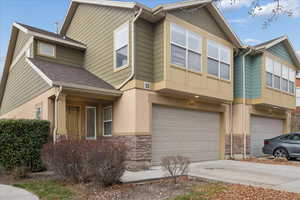 View of front of home featuring driveway, stone siding, a garage, and a shingled roof