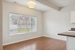 Unfurnished dining area with dark wood-style flooring and beam ceiling