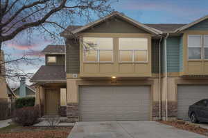 View of front of house featuring stone siding, roof with shingles, concrete driveway, and a garage