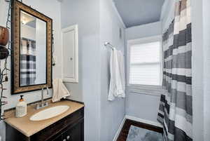 Main floor full Bathroom with vanity, a shower with curtain, dark wood-type flooring, and a textured wall