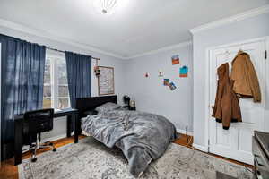 Bedroom featuring wood finished floors, ornamental molding, and an office area