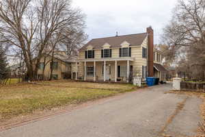 View of front of home featuring a front lawn, a porch, a chimney, driveway, and roof with shingles