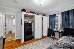 Bedroom with freestanding refrigerator, ornamental molding, wood finished floors, a desk, and a closet