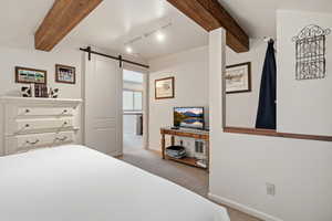 Bedroom featuring beam ceiling, a barn door, track lighting, and light carpet