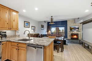 Kitchen with dishwasher, open floor plan, light stone countertops, a fireplace, and a peninsula