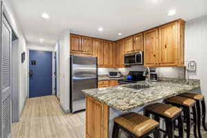 Kitchen featuring stainless steel appliances, light stone countertops, a kitchen bar, brown cabinets, and recessed lighting
