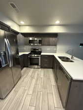 Kitchen featuring appliances with stainless steel finishes, a peninsula, wood tiled floors, dark brown cabinets, and light stone countertops