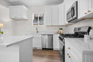Kitchen with appliances with stainless steel finishes, white cabinets, light wood-style floors, and light stone counters