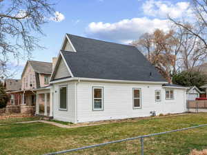 View of side of home with a shingled roof, a fenced front yard, and a porch