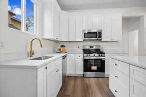 Kitchen with white cabinets, appliances with stainless steel finishes, dark wood-type flooring, and light stone counters