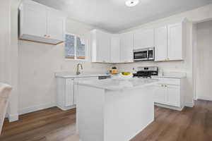Kitchen with white cabinets, stainless steel appliances, a center island, dark wood-style flooring, and light stone countertops