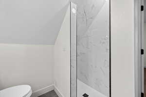 Bathroom with a marble finish shower and lofted ceiling
