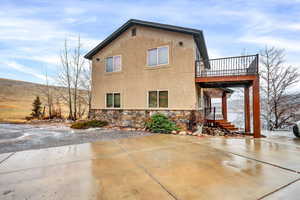 Back of house with stucco siding, stone siding, and a patio