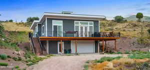 Rear view of property featuring dirt driveway, a wooden deck, a patio, and a garage