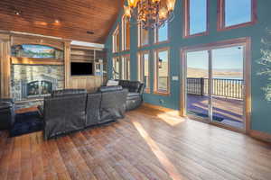 Living area with wood-type flooring, a vaulted wooden ceiling, a stone fireplace, and a chandelier