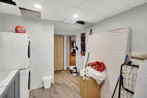 Bathroom with light wood-style flooring, recessed lighting, a drop ceiling, and stacked washer and clothes dryer