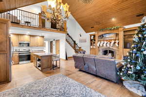 Living area featuring recessed lighting, high vaulted ceiling, light wood finished floors, a chandelier, and a stone fireplace